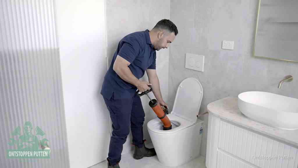 Een monteur buigt over een wandcloset en duwt met de hand een persluchtontstopper in de toiletpot om de verstopping handmatig los te maken in Putten