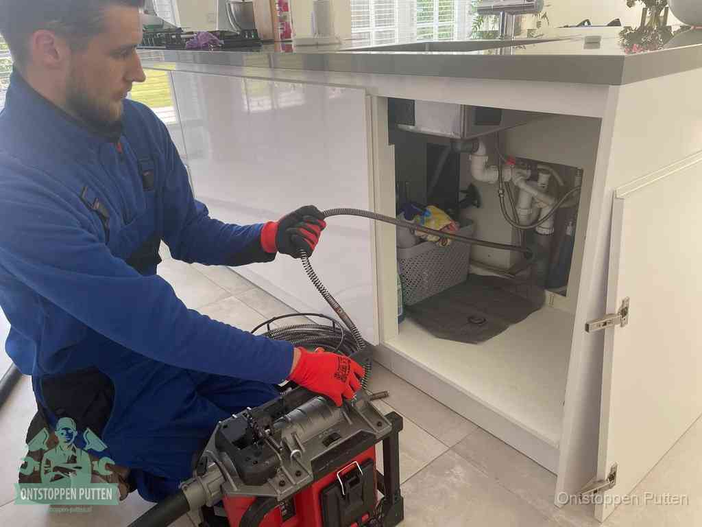 Monteur voert een ontstoppingsveer in de afvoer onder de keuken in Putten