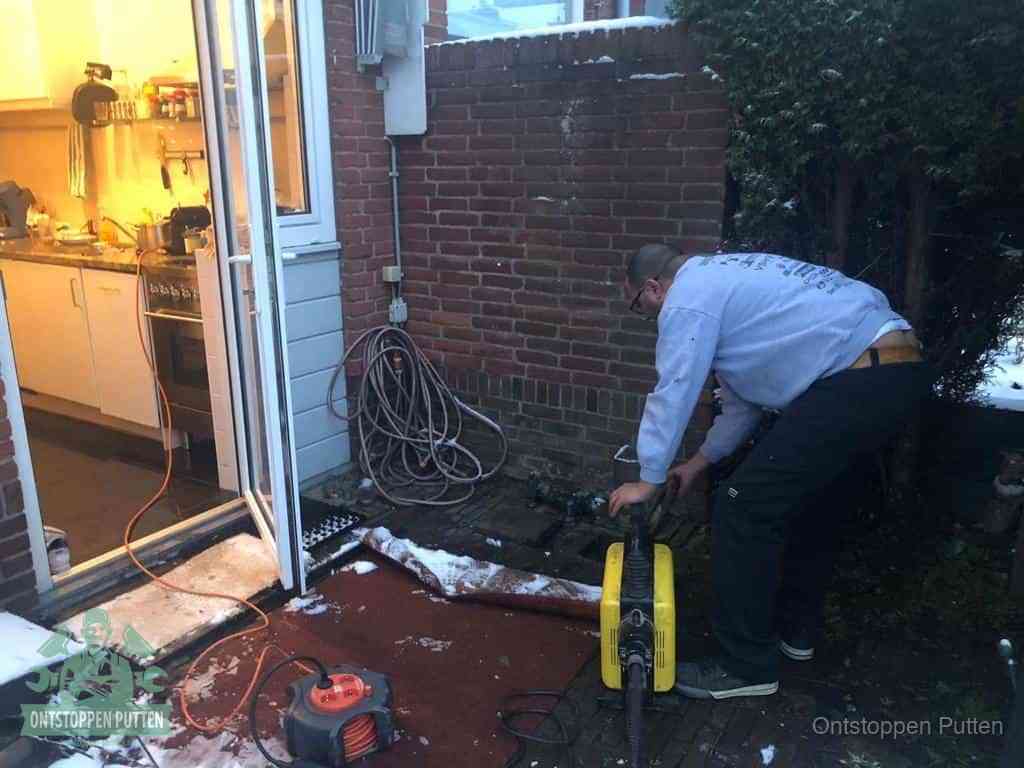 Een monteur werkt buiten bij een open riool-/grondput met een elektrische ontstoppingsmachine om een verborgen afvoerprobleem op te sporen in Putten