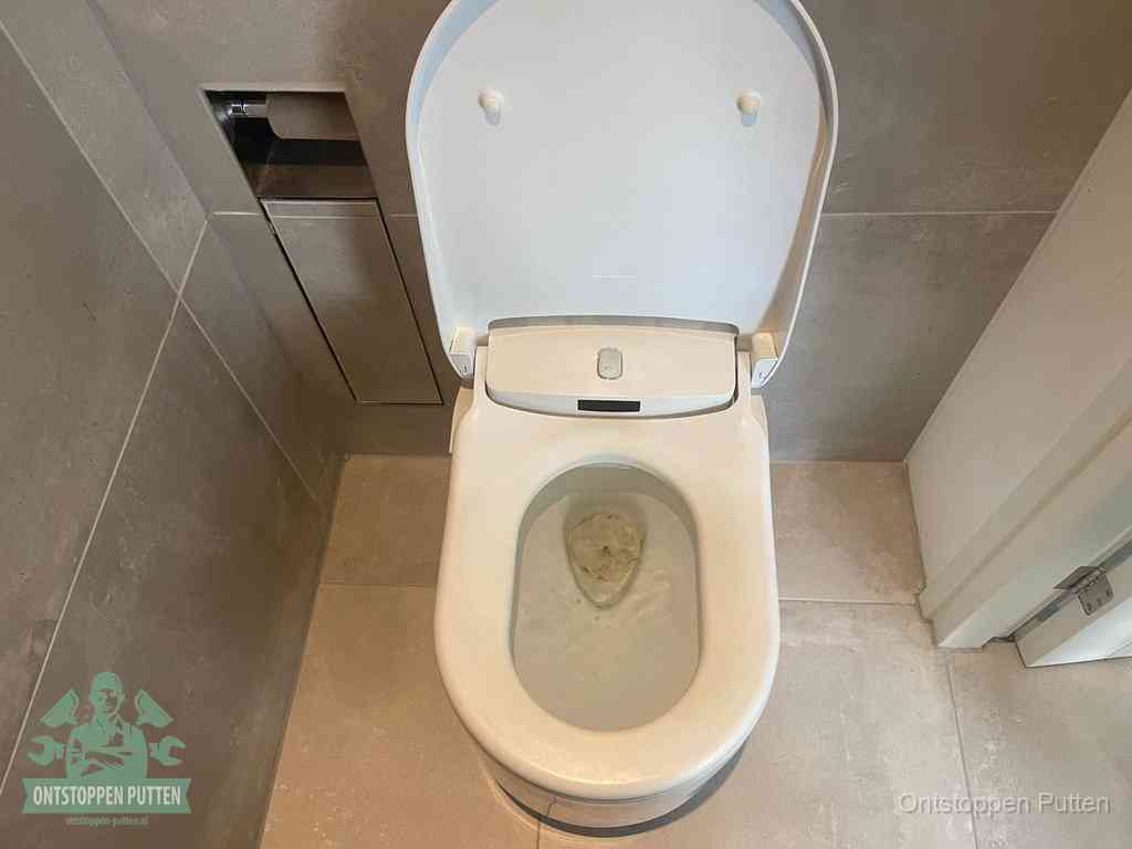 Een wit hangtoilet waarin een prop wc-papier op het water blijft drijven, een duidelijk signaal van een verstopte wc in Putten