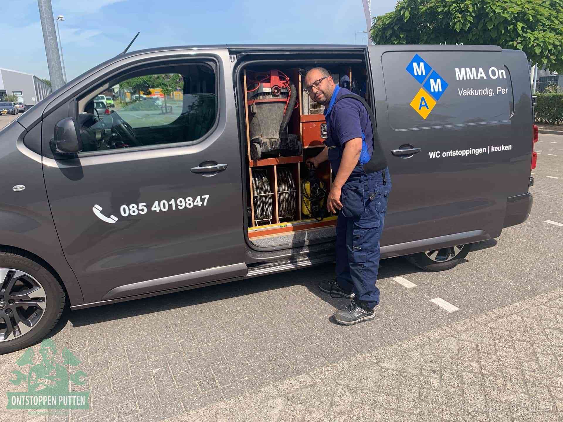 Een monteur bij de open schuifdeur van zijn bedrijfsbus op een parkeerplaats, klaar om de oorzaak van terugkerende afvoerverstoppingen aan te pakken in Putten