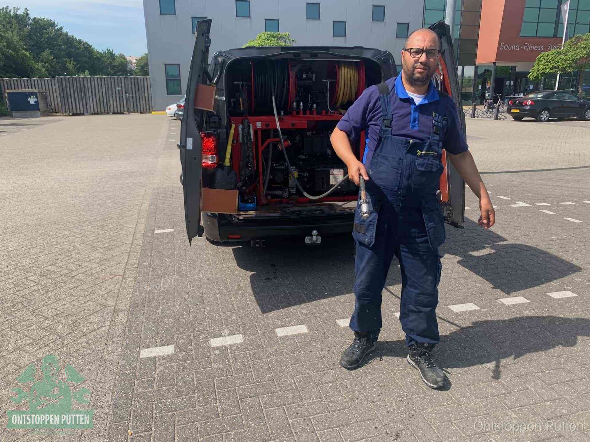 Een monteur bij zijn bestelbus met een hogedruk- en rioolreinigingsunit, klaar om de oorzaak van terugkerende wc-verstoppingen aan te pakken in Putten