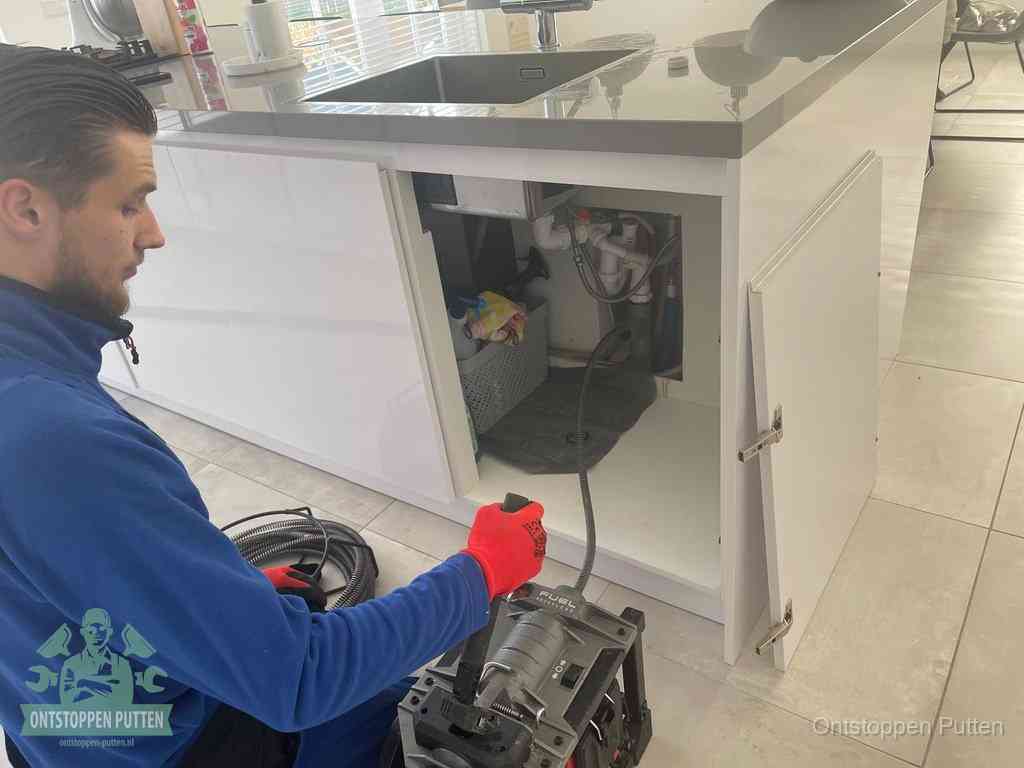 Monteur ontstopt met een veermachine een verstopte afvoer onder de gootsteen in Putten