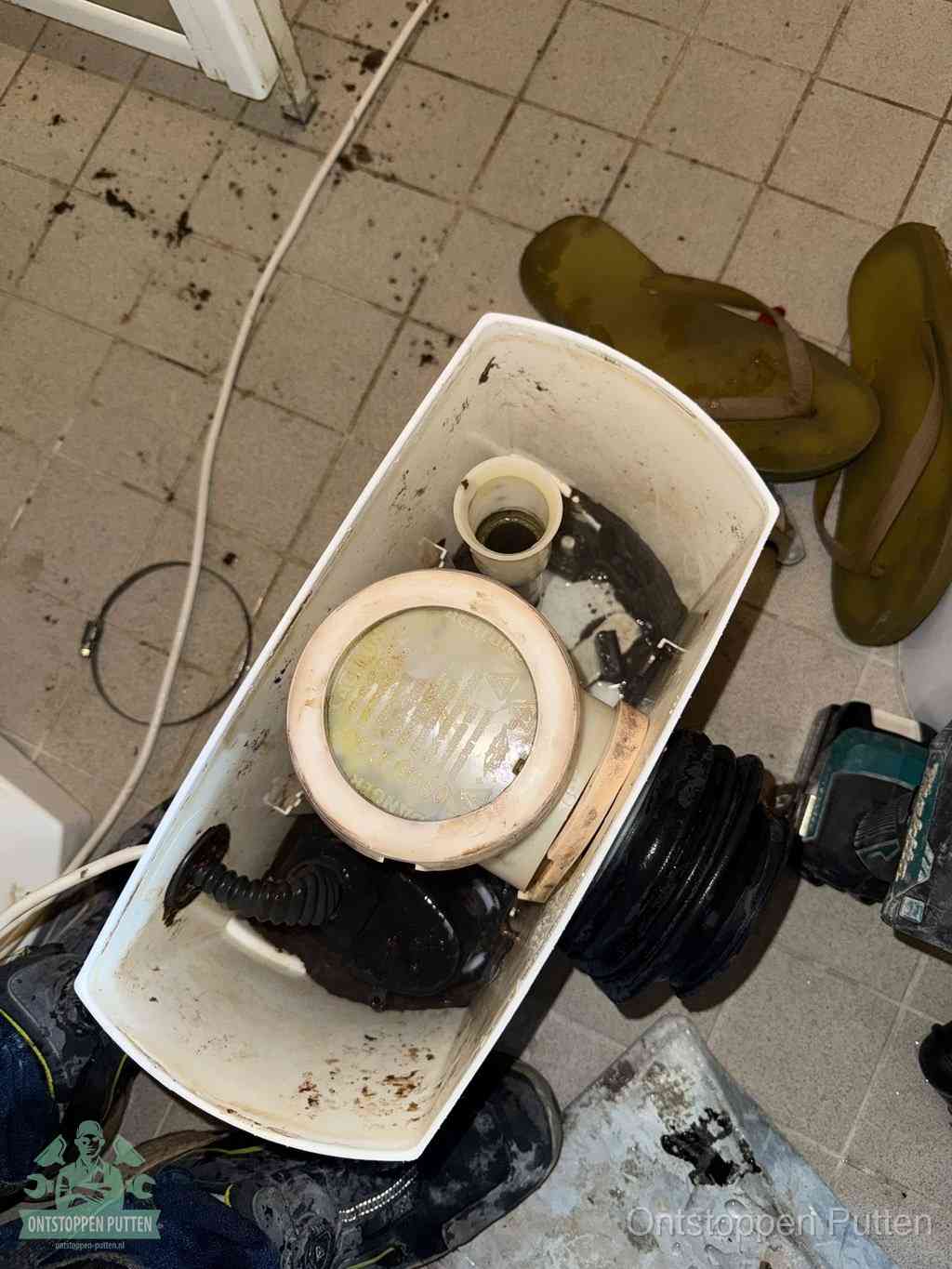 Een gedemonteerde toiletpot op de vloer met ontstoppingsveer en gereedschap ernaast, het verwijderen van een vastzittend voorwerp uit de wc in Putten