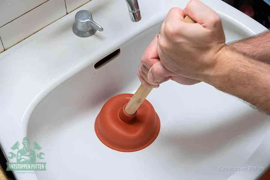 Twee handen gebruiken een rode rubberen plopper op een sanitair-afvoer om het toilet te ontstoppen in Putten
