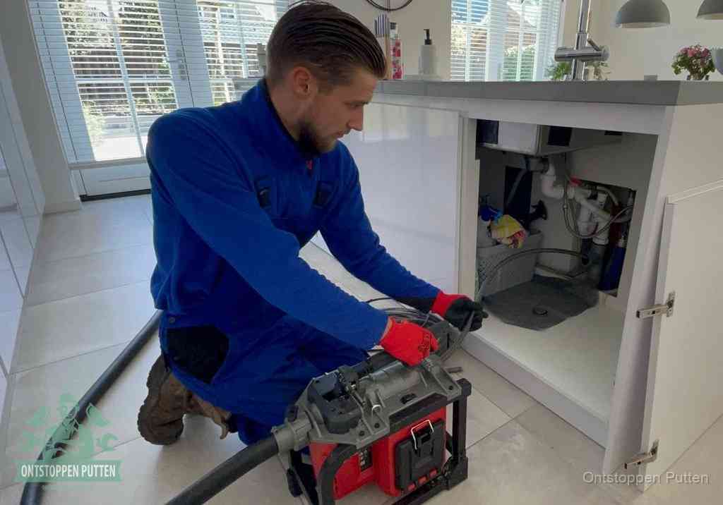 Een monteur voert een professionele elektrische ontstoppingsmachine in de afvoer onder de spoelbak tijdens het gootsteen ontstoppen in Putten