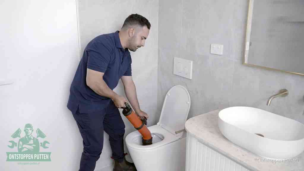 Een man gebruikt een handmatige luchtdruk-ontstopper in een modern betegeld toilet om zelf de wc te ontstoppen in Putten